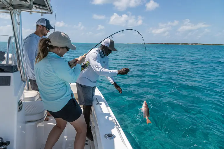 Guest reeling in a small reef fish with help from the captain
